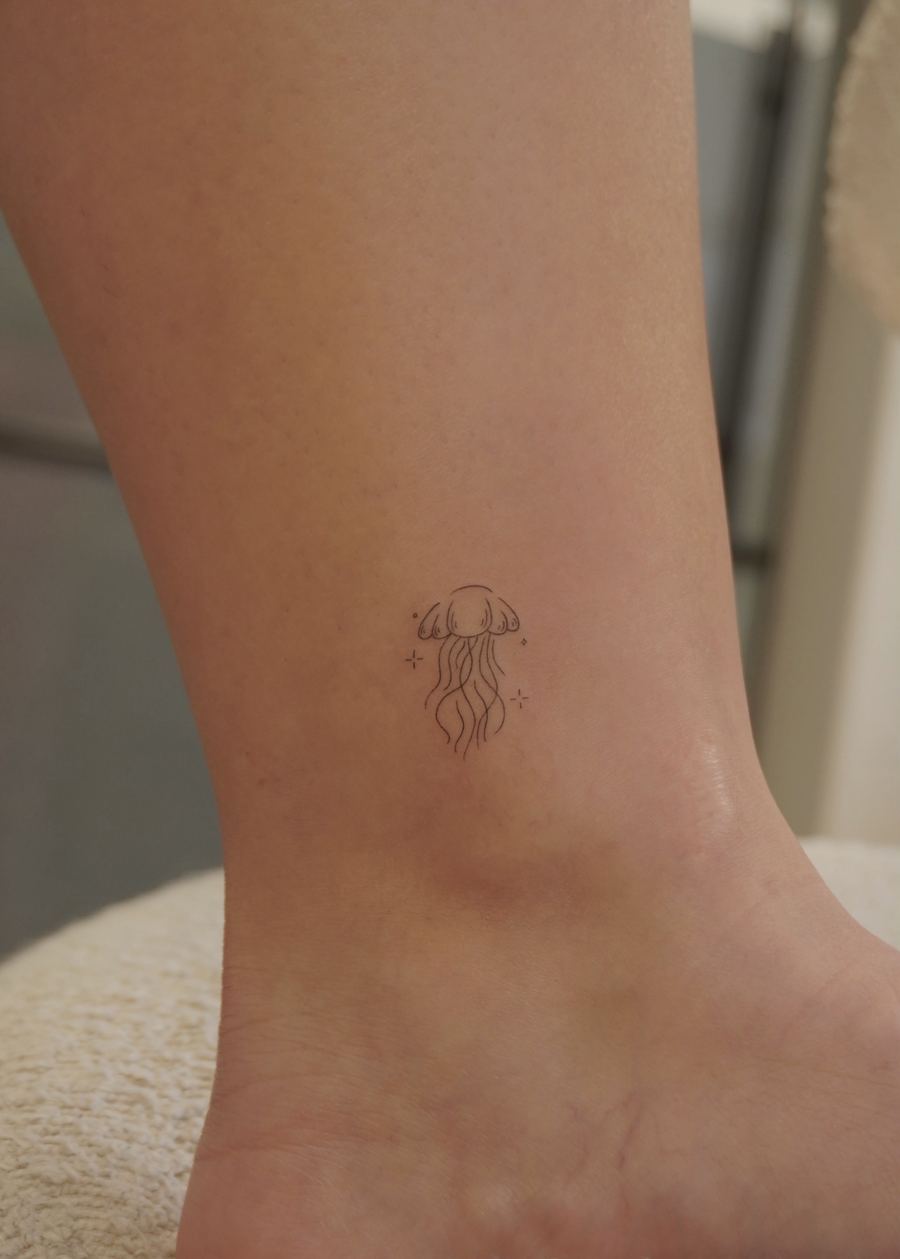 Tatuaje fine line de una medusa minimalista con destellos, tobillo