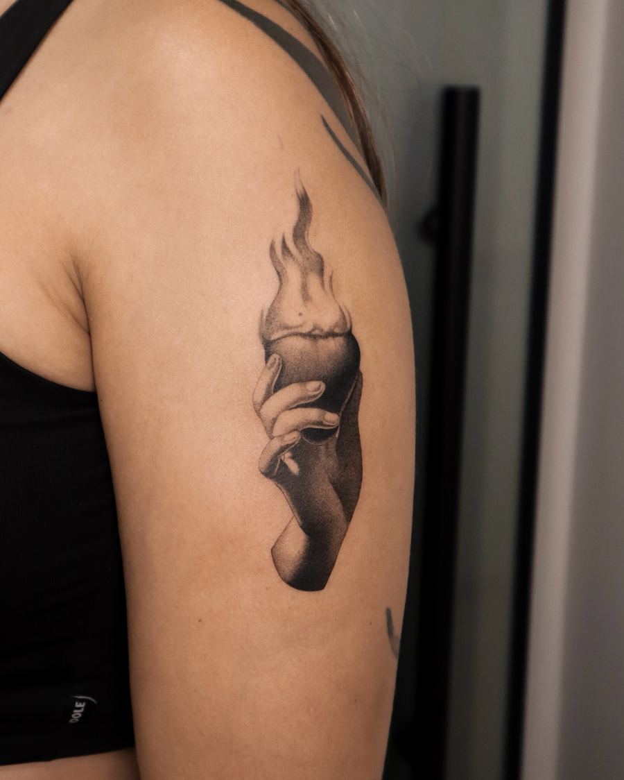 Tatuaje black and grey de una mano sosteniendo una vela encendida, brazo